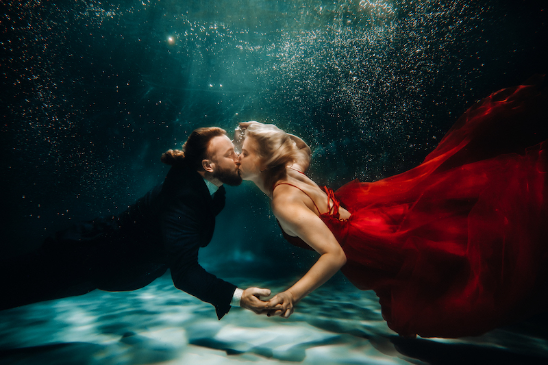 Paar in Anzug und Kleid küssen sich unter Wasser
