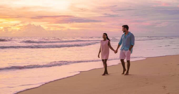Paar spaziert Händchen haltend bei Sonnenuntergang am Strand entlang