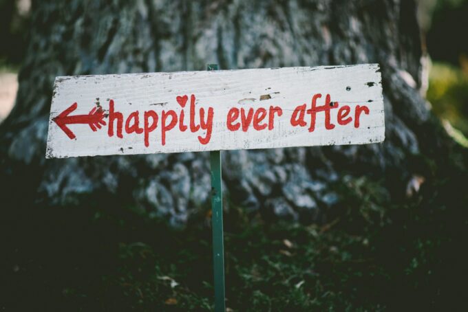 Ein Holzschild mit der Aufschrift „Happy Ever After“ vor einem Baum.