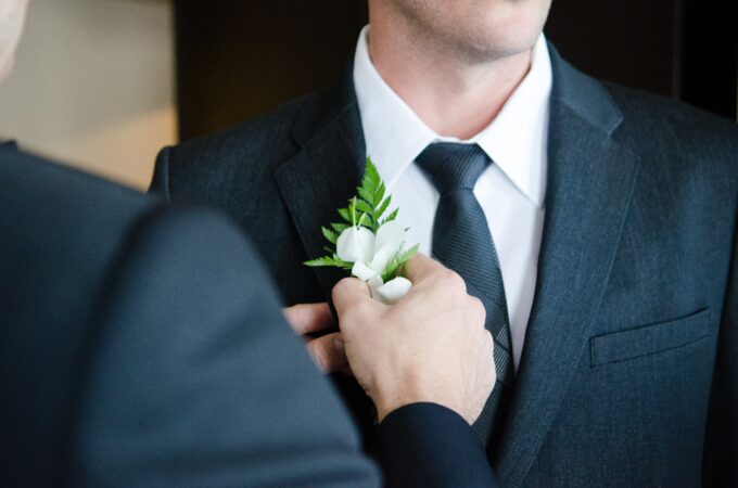 Ein Mann im Anzug steckt sich eine Ansteckblume an.