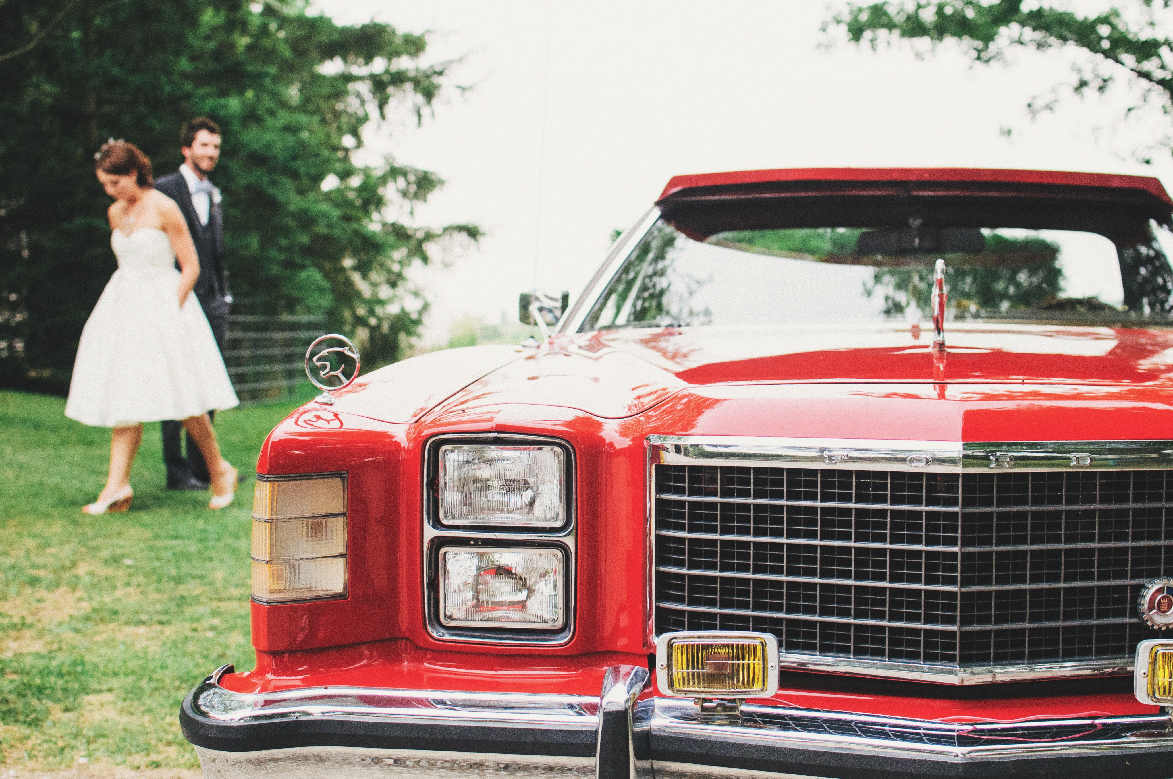 Eine Braut und ein Bräutigam stehen neben einem roten Auto.