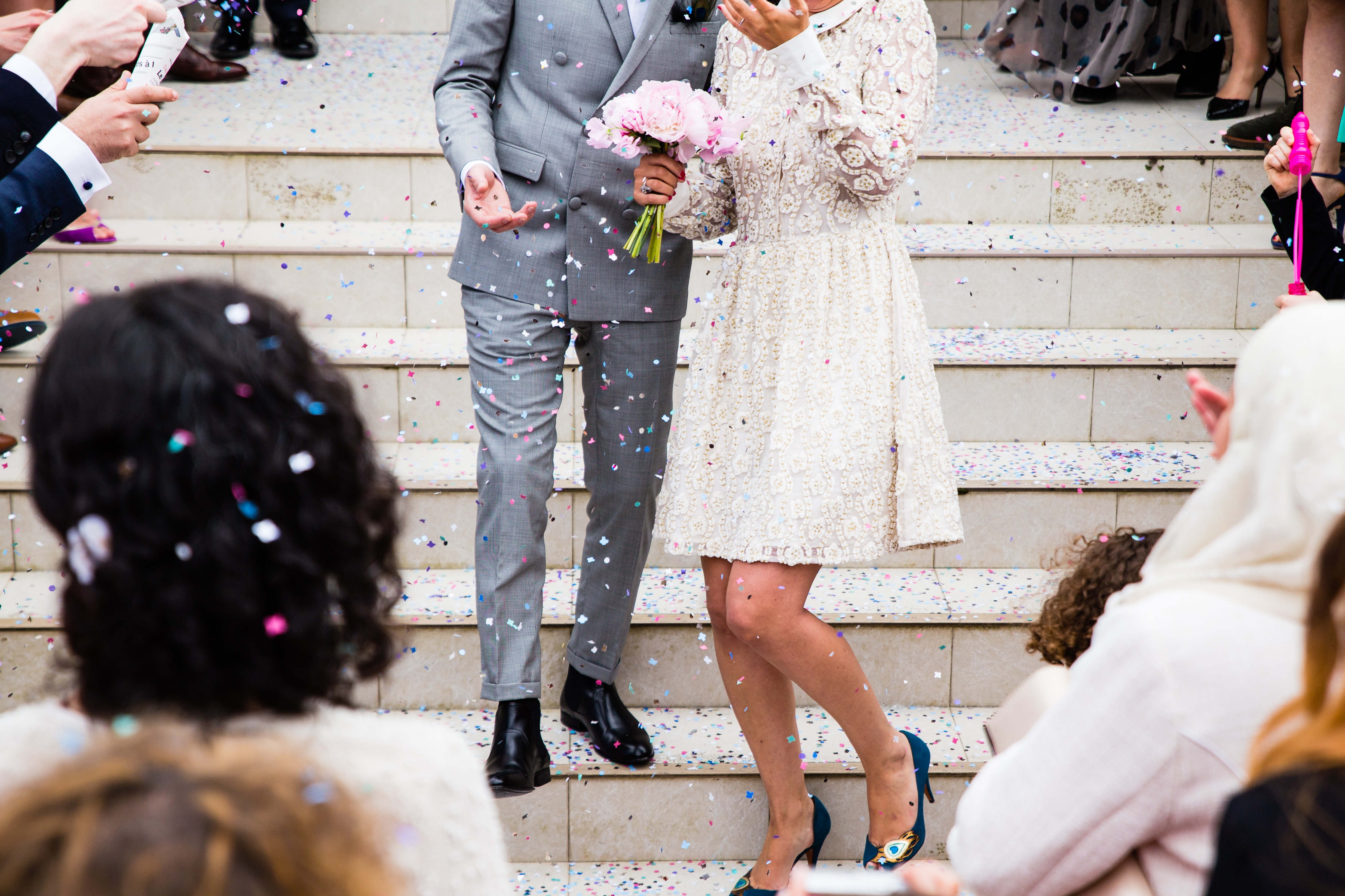 Eine Braut und ein Bräutigam stehen auf Stufen und werden mit Konfetti beworfen.