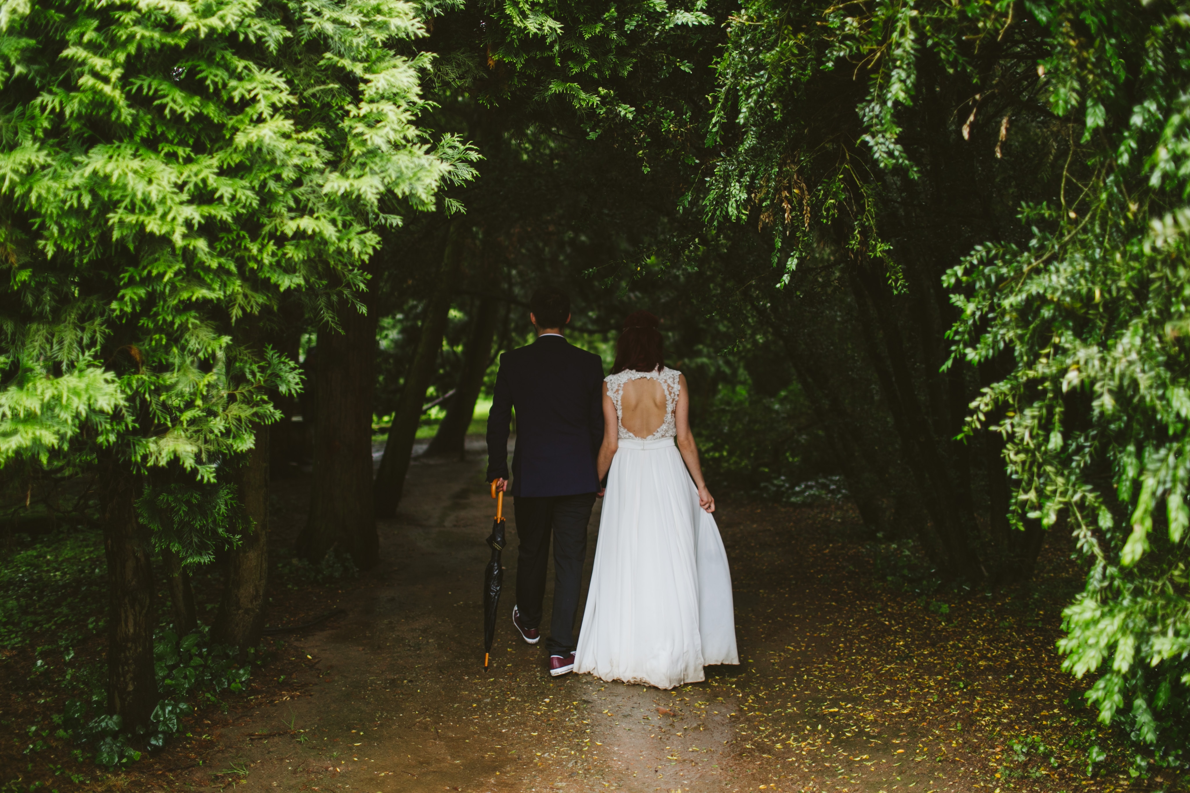 Eine Braut und ein Bräutigam gehen einen Pfad in einem Wald entlang.