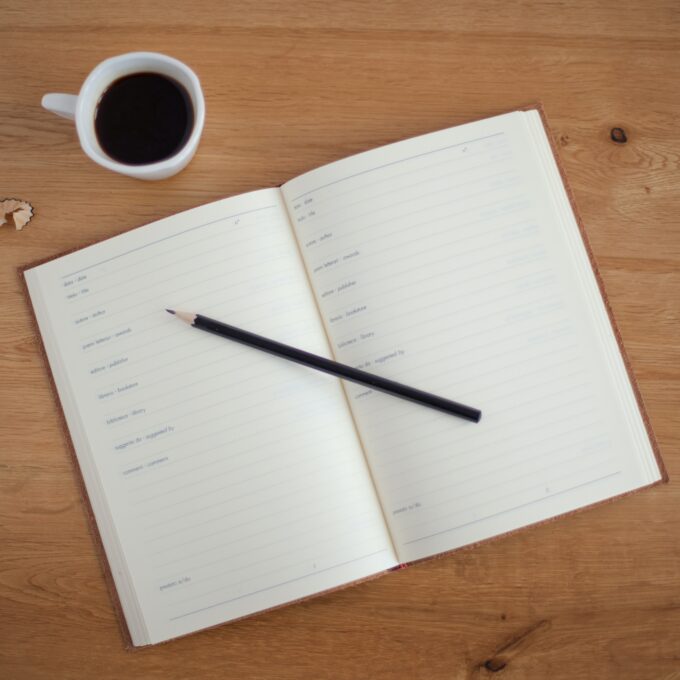 Ein Notizbuch mit Bleistift und einer Tasse Kaffee auf einem Holztisch.