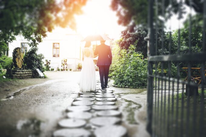 Eine Braut und ein Bräutigam gehen mit einem Regenschirm einen Kopfsteinpflasterweg entlang.