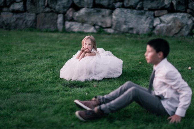 Ein kleines Mädchen sitzt im Gras neben einem Mann im Anzug.