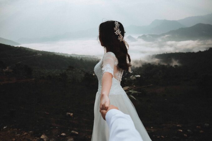 Eine Braut und ein Bräutigam halten sich in den Bergen an den Händen.