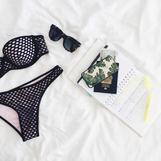 Ein Paar Bikinis, eine Sonnenbrille und ein Notizbuch auf einem Bett.