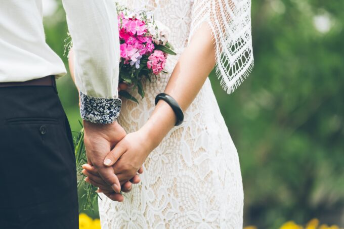 Eine Braut und ein Bräutigam halten sich in einem Park an den Händen.