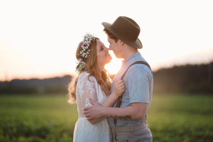 Eine Braut und ein Bräutigam umarmen sich bei Sonnenuntergang auf einem Feld.