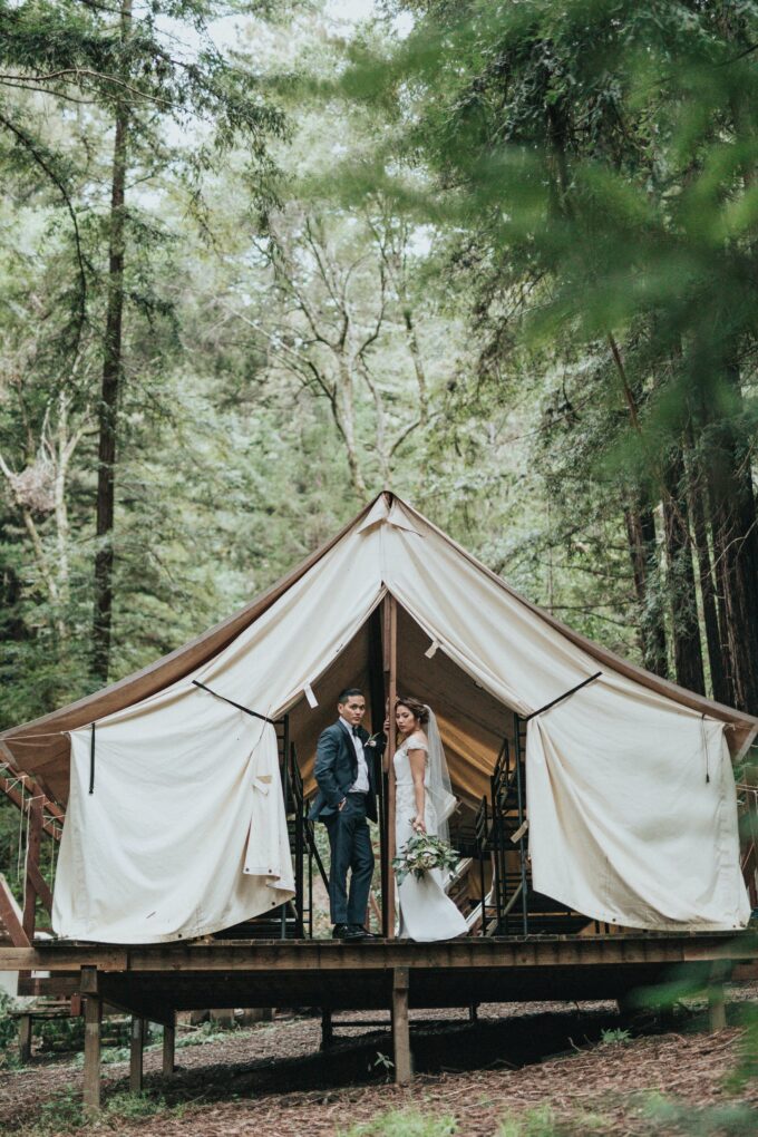 Ein Brautpaar steht vor einem Zelt im Wald.