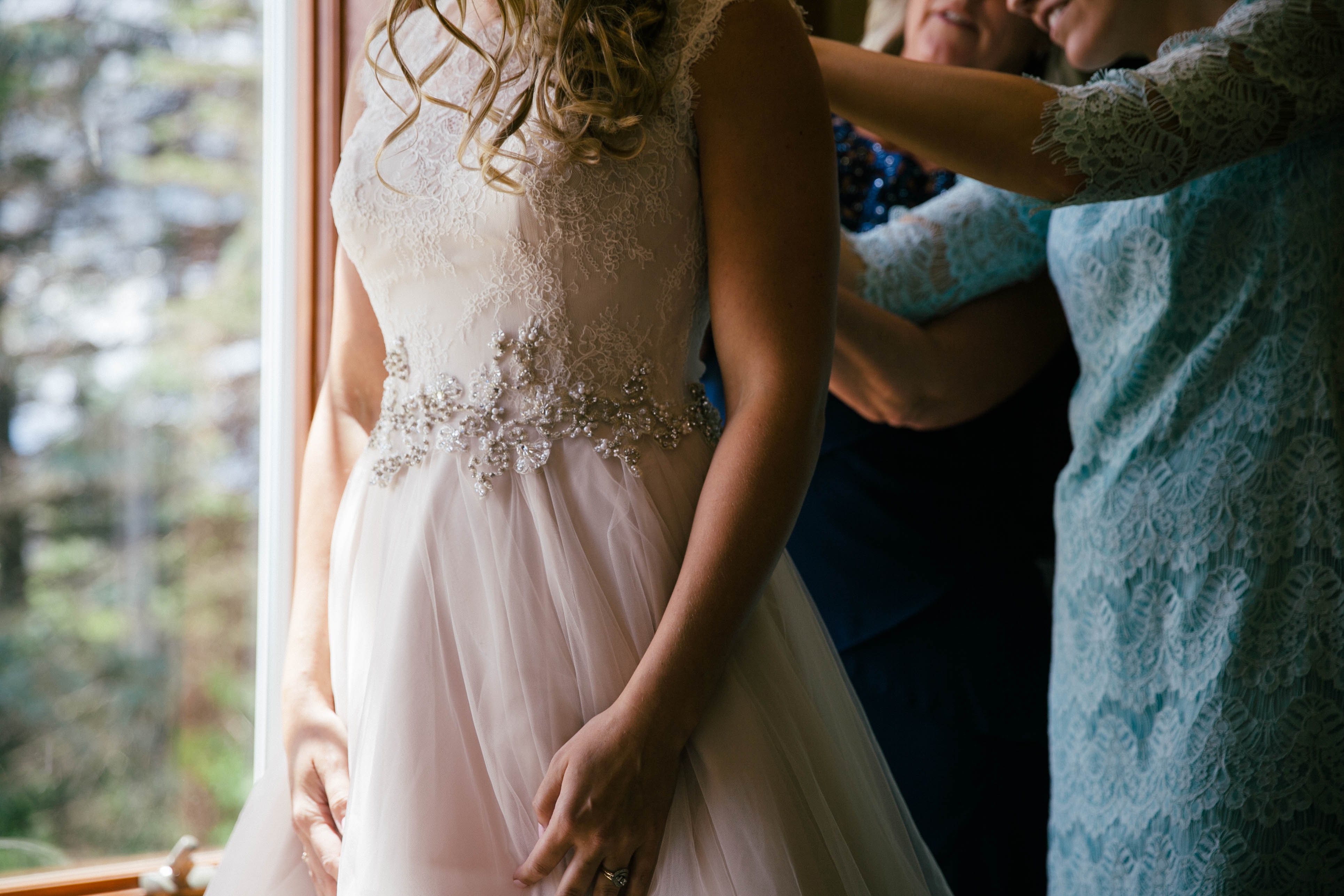 Eine Braut bereitet vor einem Fenster ihr Hochzeitskleid vor.