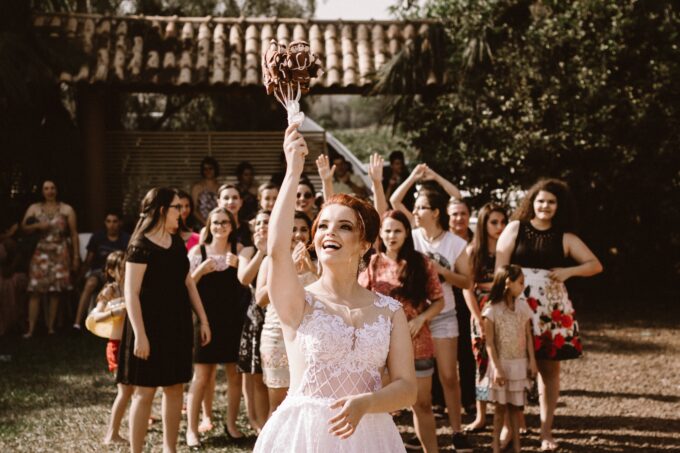 Eine Braut in einem Hochzeitskleid hält einen Blumenstrauß in die Luft.