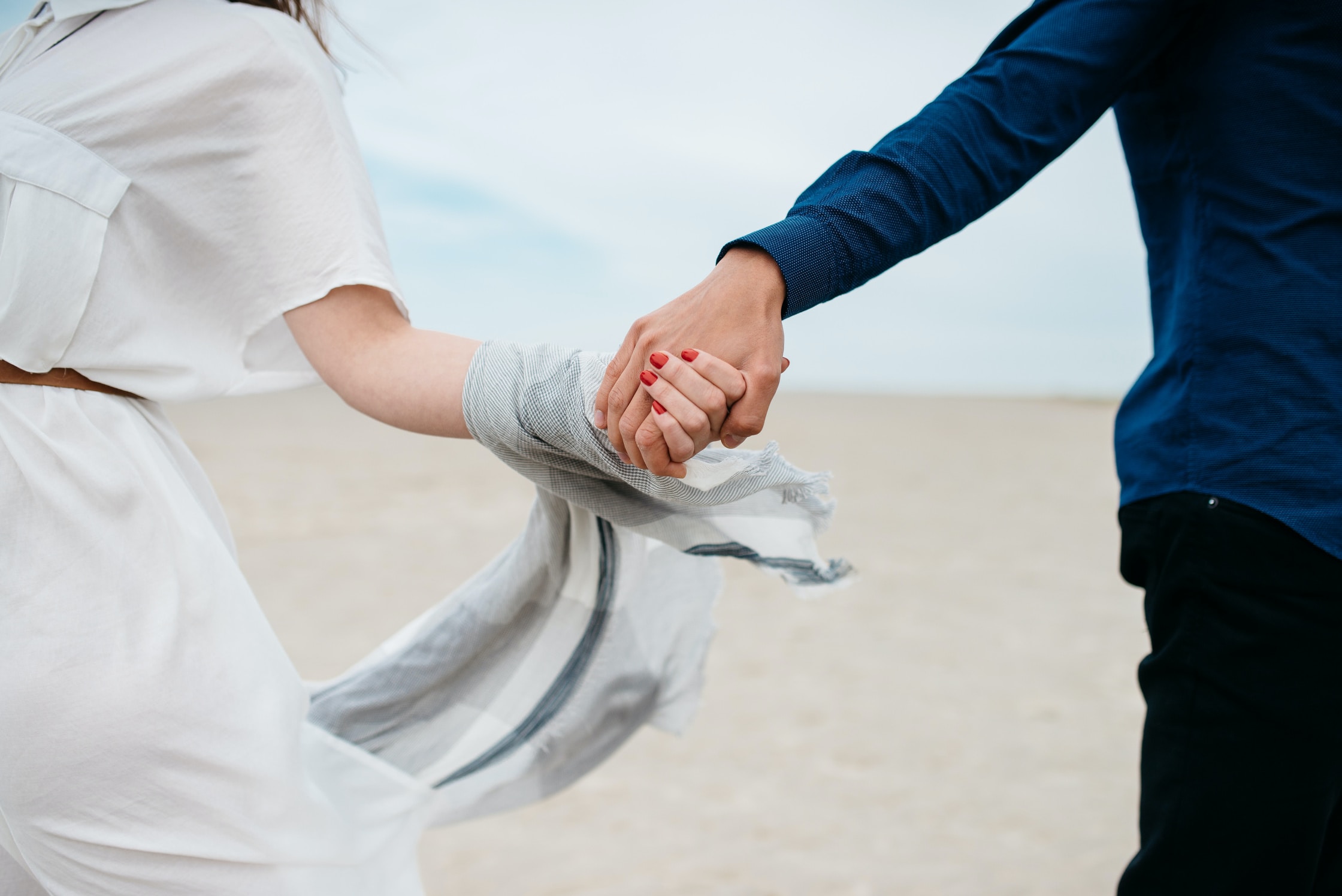 Ein Mann und eine Frau halten sich an den Händen, während sie am Strand spazieren gehen.