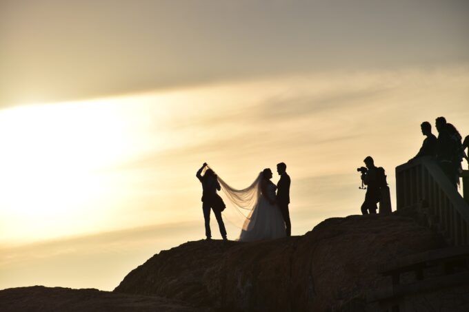 Eine Braut und ein Bräutigam stehen bei Sonnenuntergang auf einem Felsen.