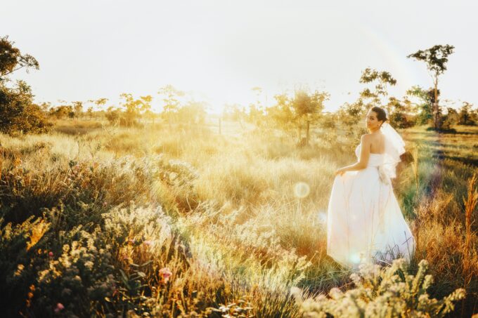 Eine Braut in einem Hochzeitskleid steht bei Sonnenuntergang auf einem Feld.