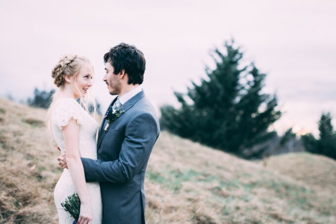 Eine Braut und ein Bräutigam umarmen sich auf einem Hügel.