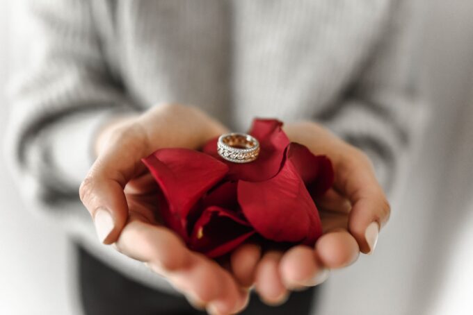 Die Hände einer Frau halten einen Ehering und eine rote Rose.