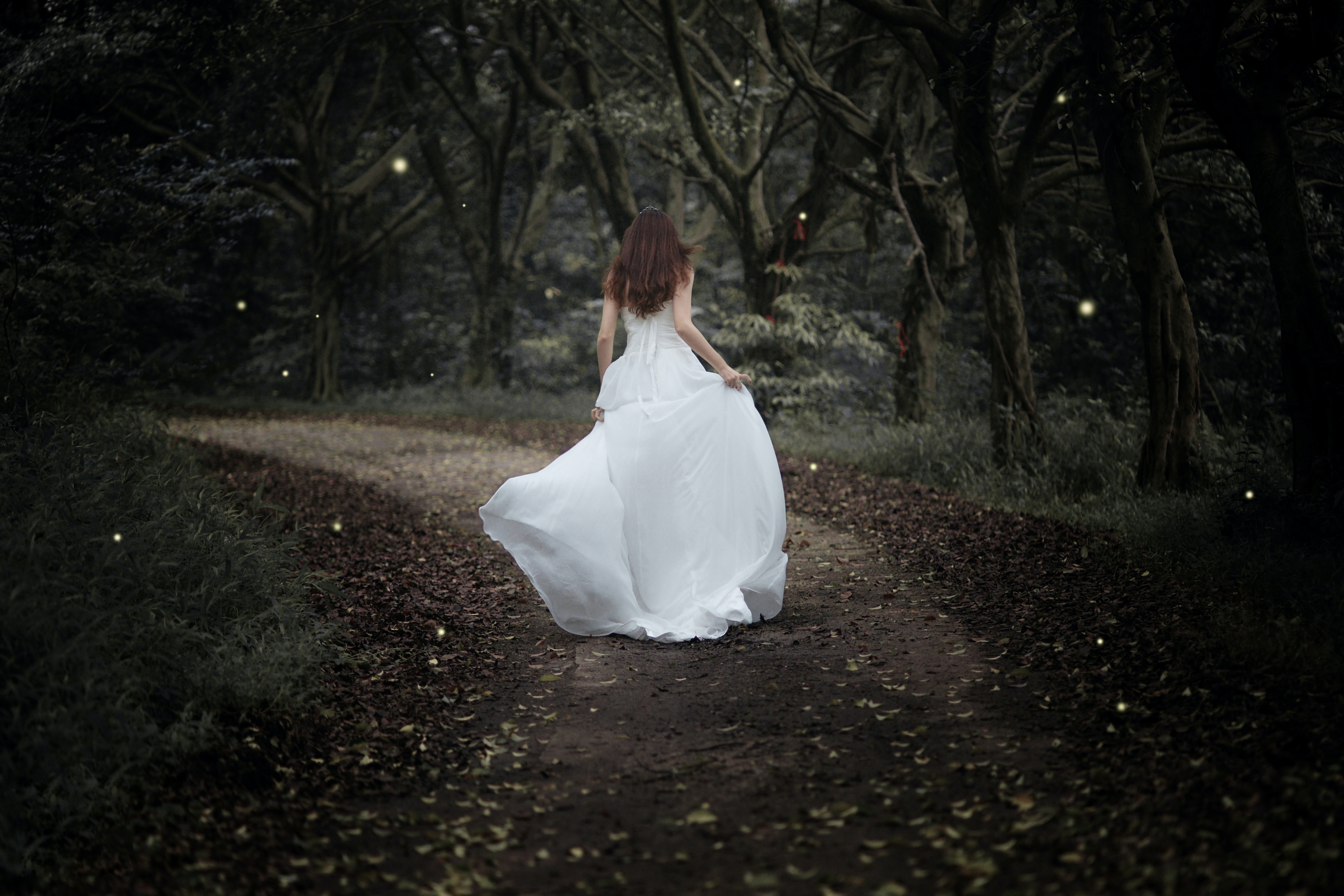 Eine Frau in einem weißen Kleid geht einen Pfad im Wald entlang.