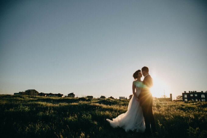 Eine Braut und ein Bräutigam stehen auf einem Feld und die Sonne geht hinter ihnen unter.