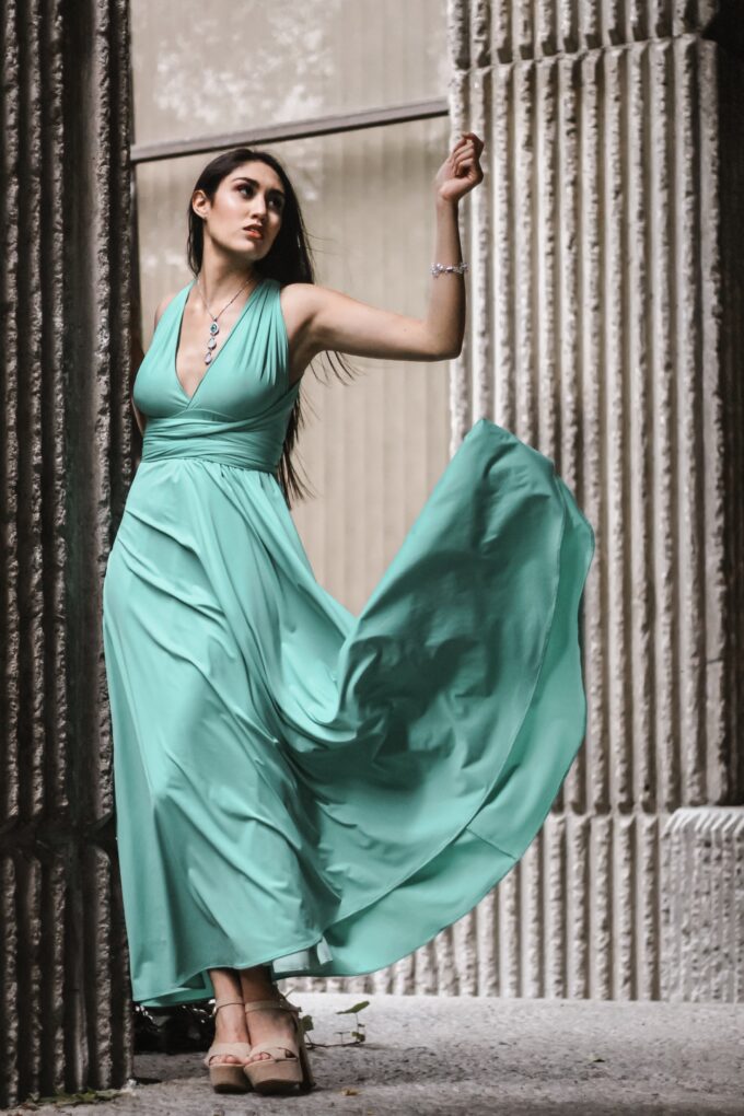 Eine Frau in einem türkisfarbenen Kleid posiert vor Säulen.