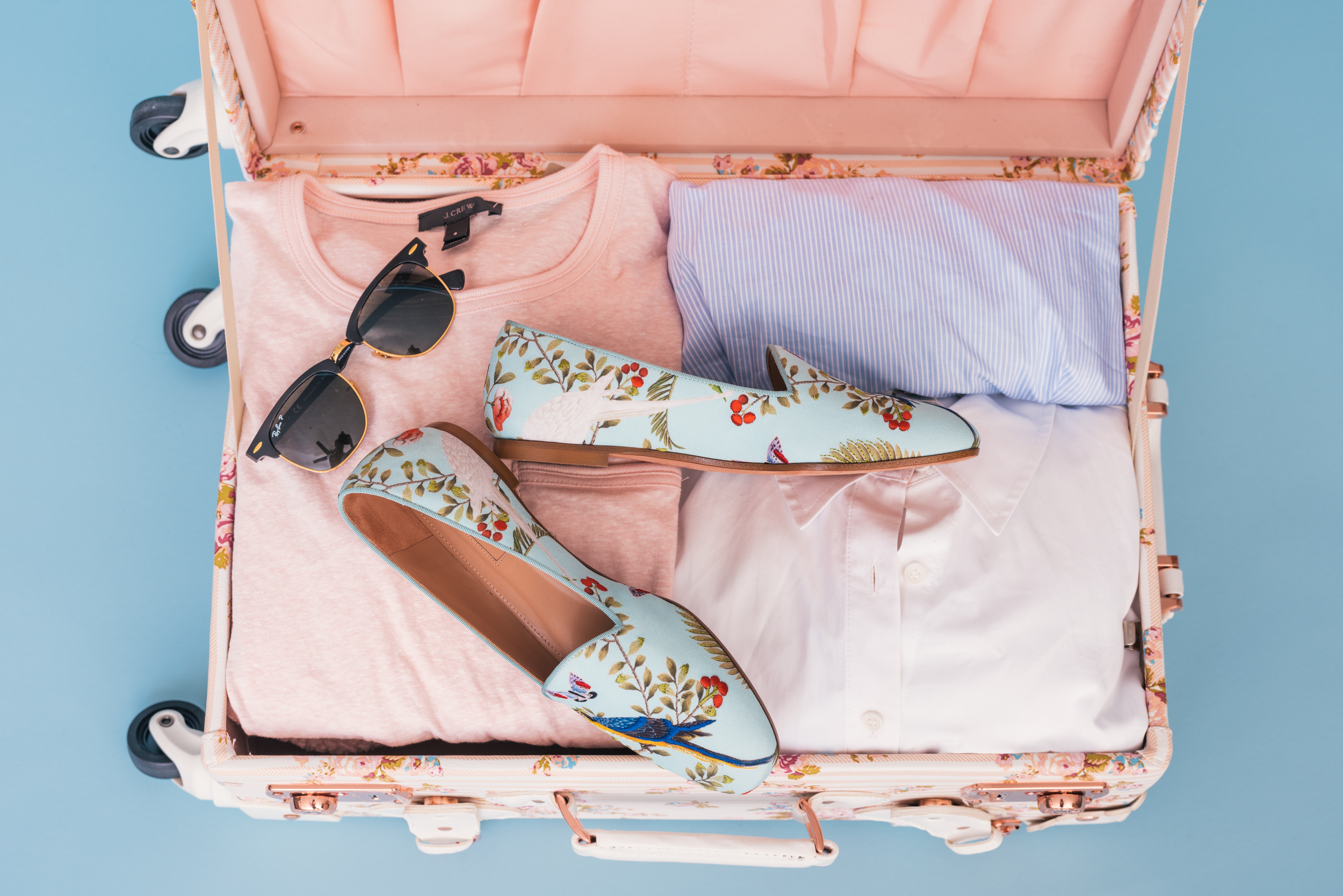 Ein Koffer voller Kleidung und Schuhe auf blauem Hintergrund.