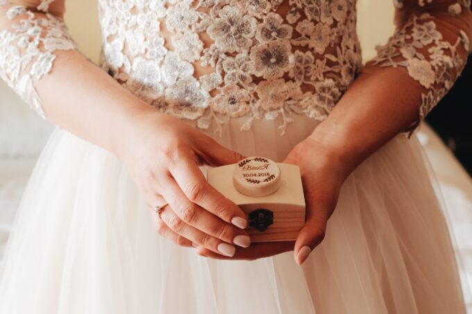 Eine Braut in einem Hochzeitskleid hält eine Holzkiste.