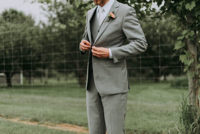 Ein Bräutigam im grauen Anzug steht auf einem Feld.