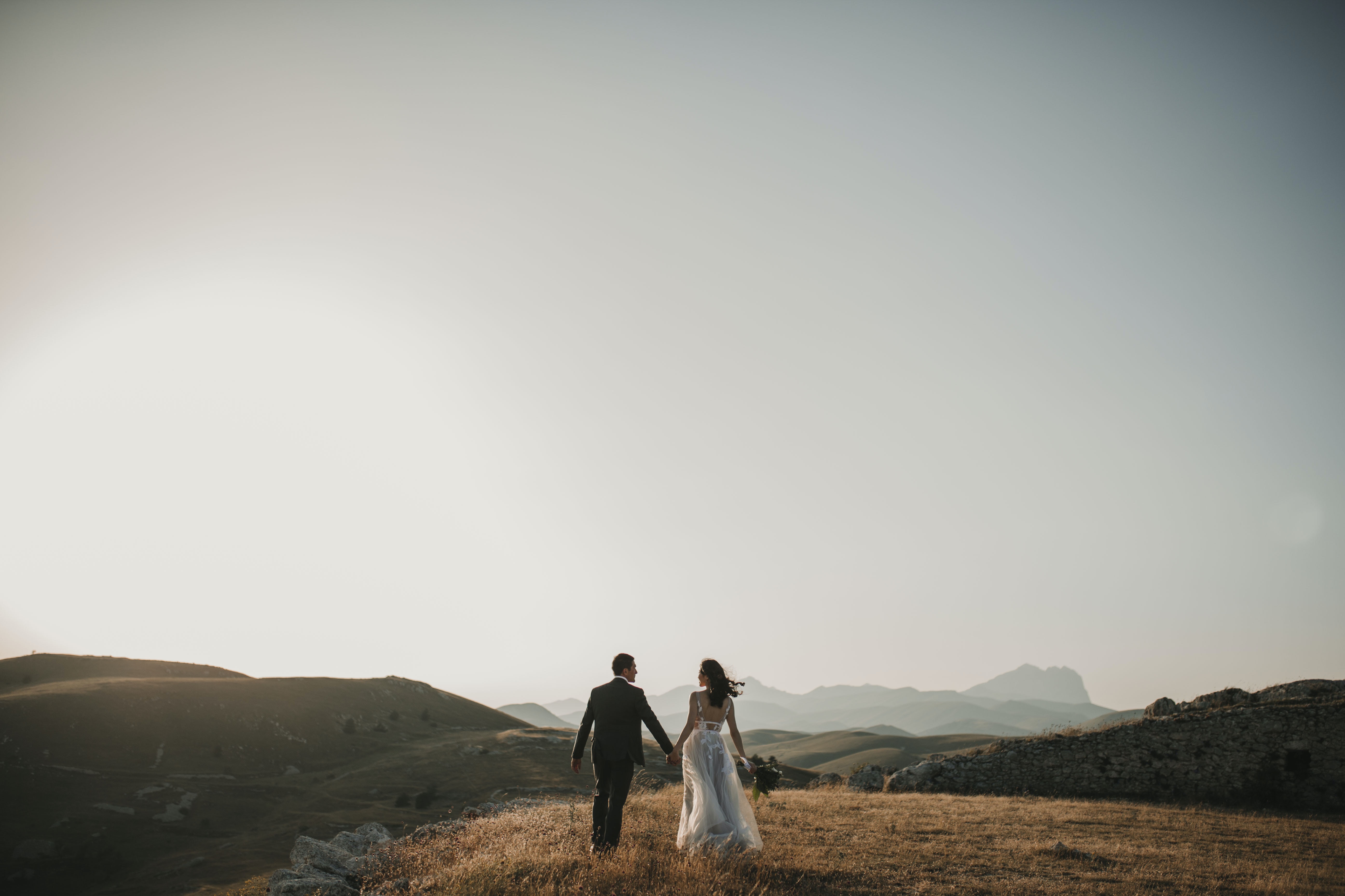 Eine Braut und ein Bräutigam stehen auf einem Hügel mit Bergen im Hintergrund.