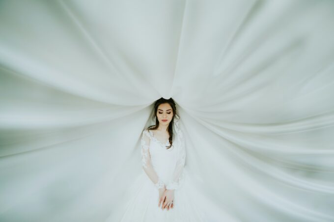 Eine Braut in einem weißen Kleid steht unter einem weißen Vorhang.