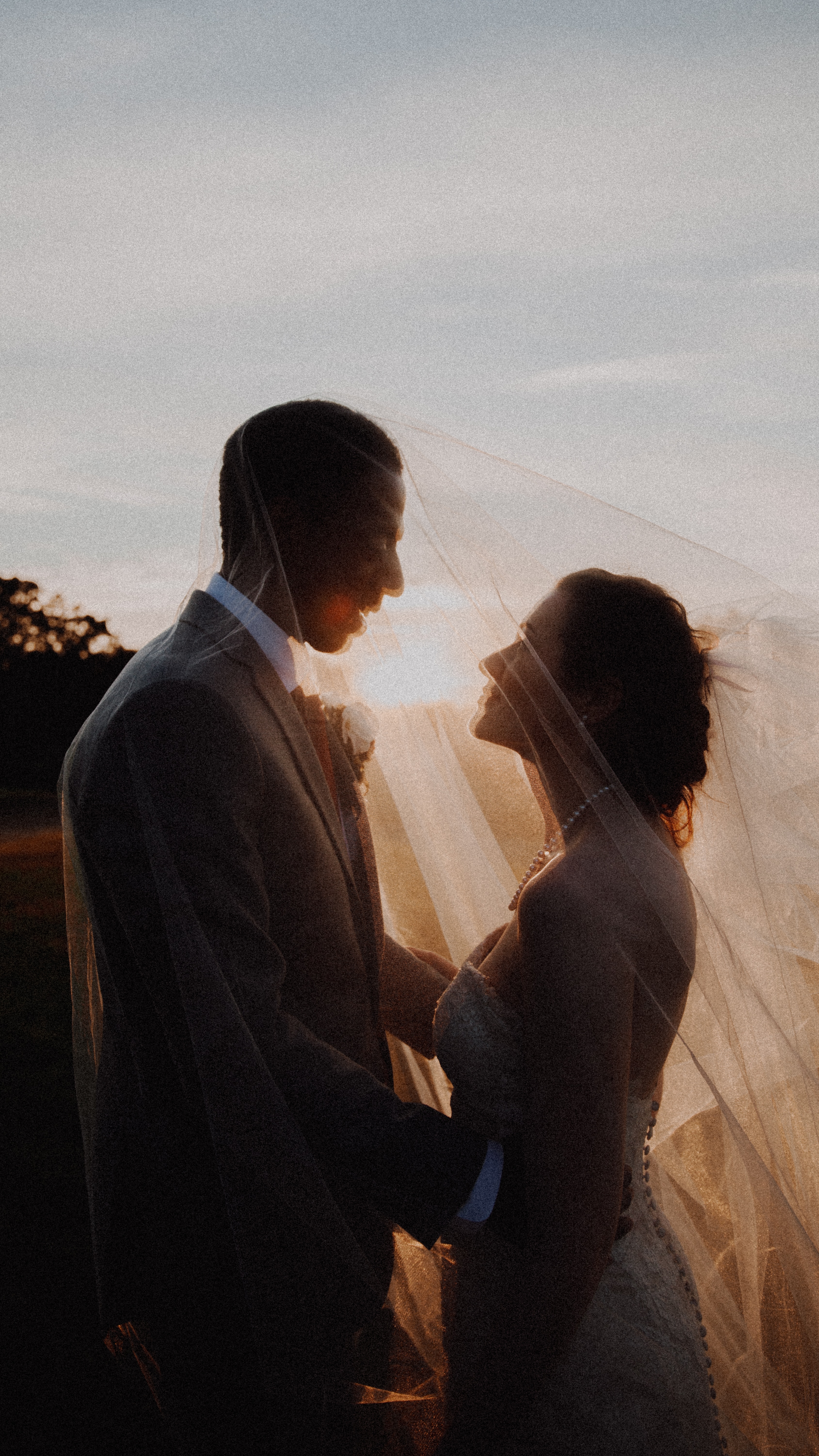 Eine Braut und ein Bräutigam stehen bei Sonnenuntergang unter einem Schleier.