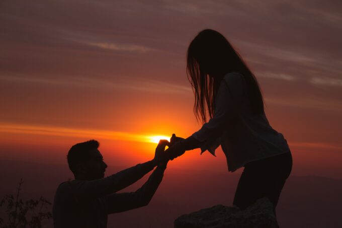 Ein Mann macht einer Frau auf einem Berggipfel einen Heiratsantrag.