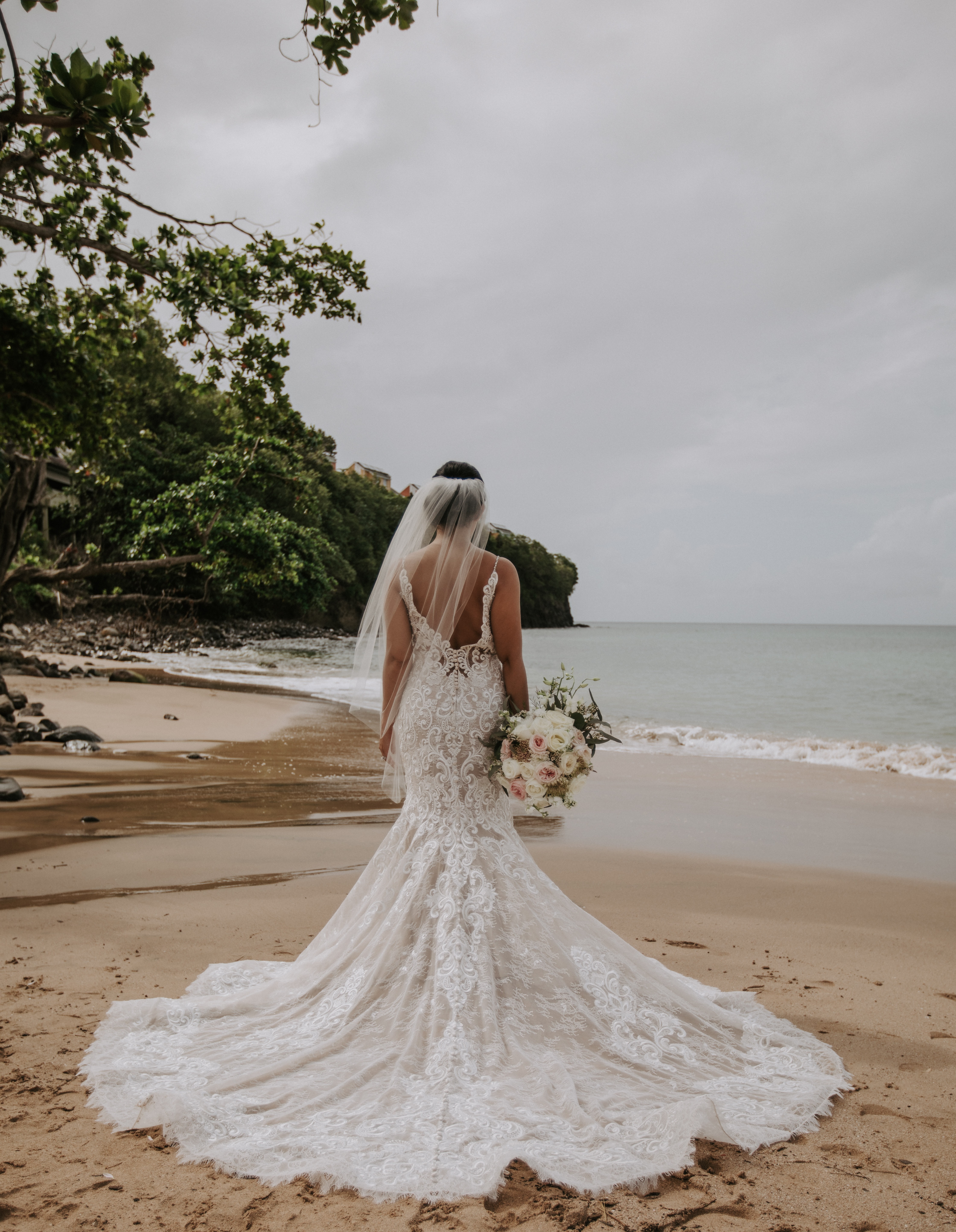 Eine Braut steht in ihrem Hochzeitskleid am Strand.