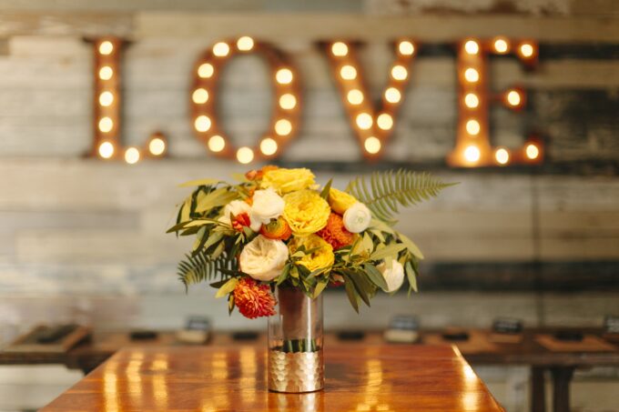 Eine Vase mit Blumen auf einem Tisch vor einem Schild mit der Aufschrift „Liebe“.