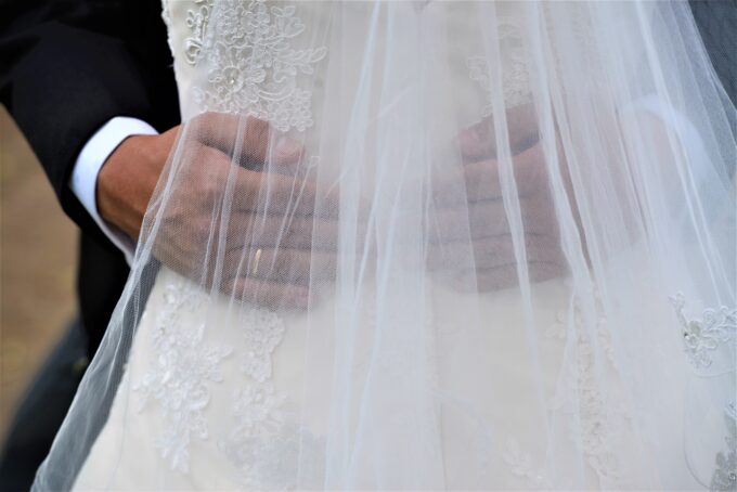 Eine Braut und ein Bräutigam halten sich in einem Hochzeitskleid an den Händen.