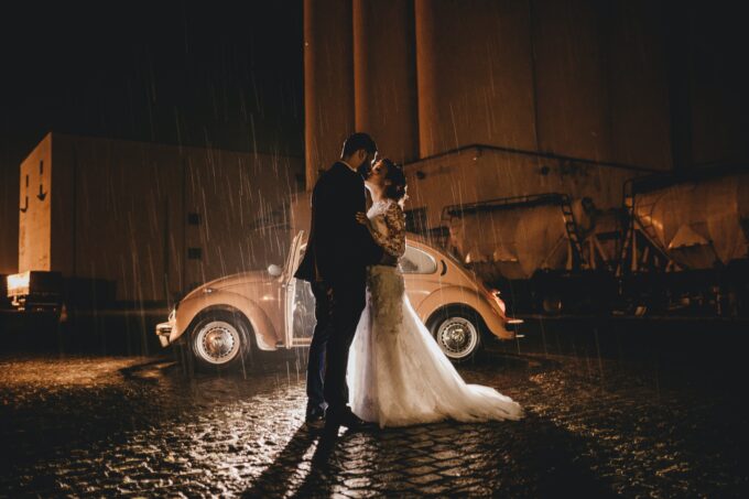 Ein Brautpaar steht im Regen vor einem Auto.