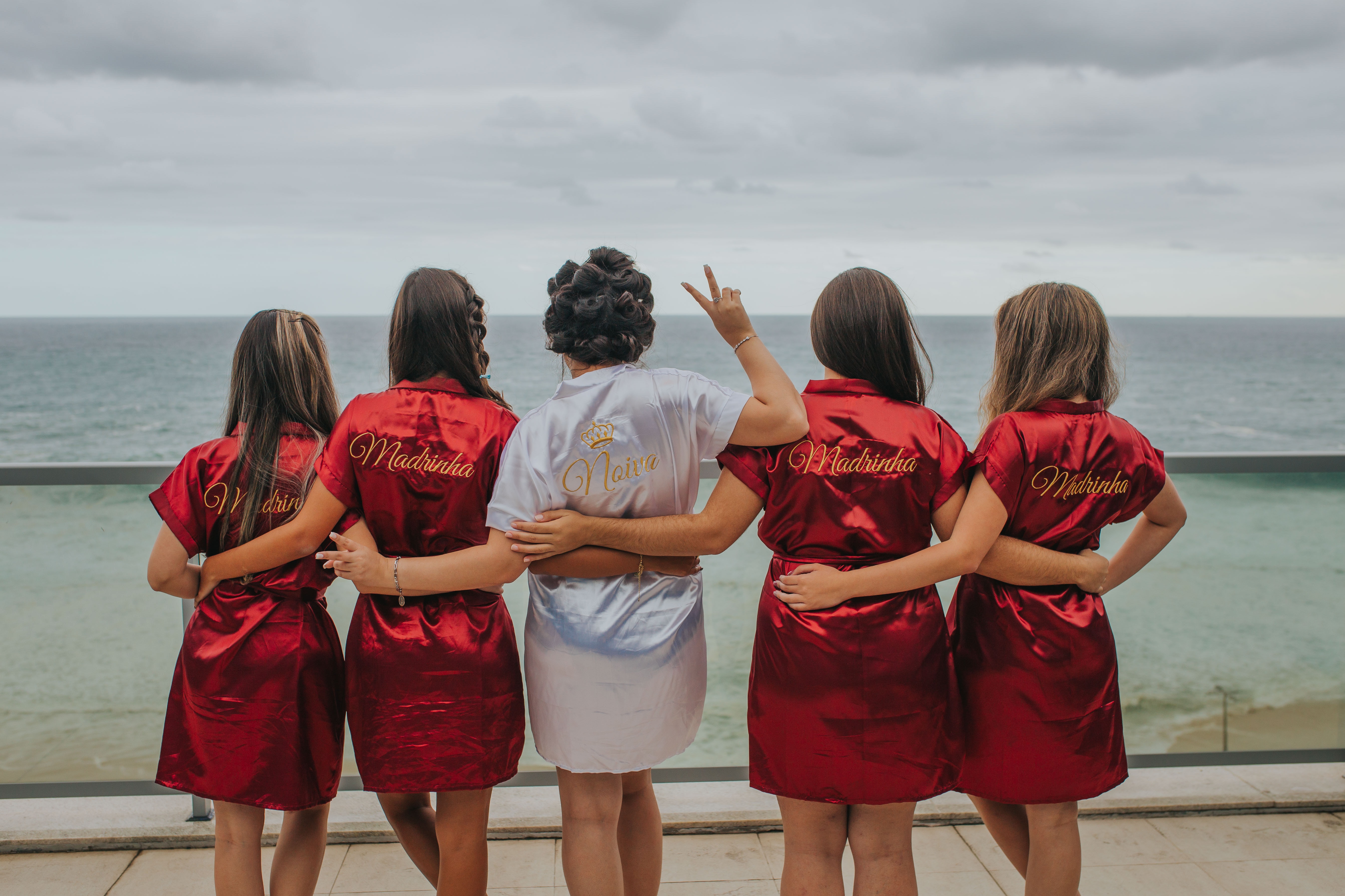 Brautjungfern in roten Gewändern stehen auf einem Balkon mit Blick auf den Ozean.