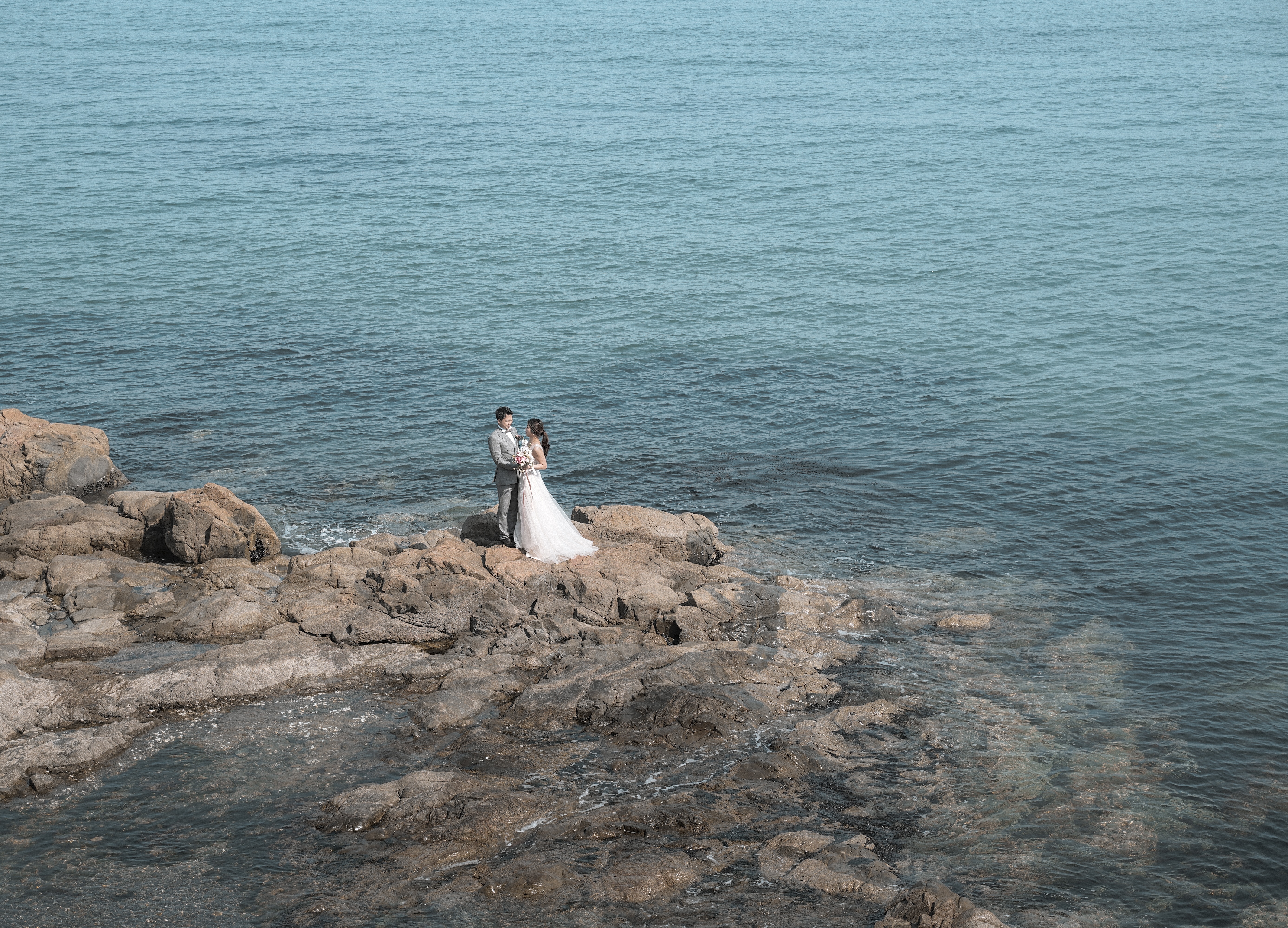 Eine Braut und ein Bräutigam stehen auf Felsen am Meer.