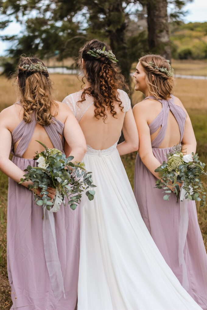 Drei Brautjungfern in lavendelfarbenen Kleidern stehen auf einem Feld.