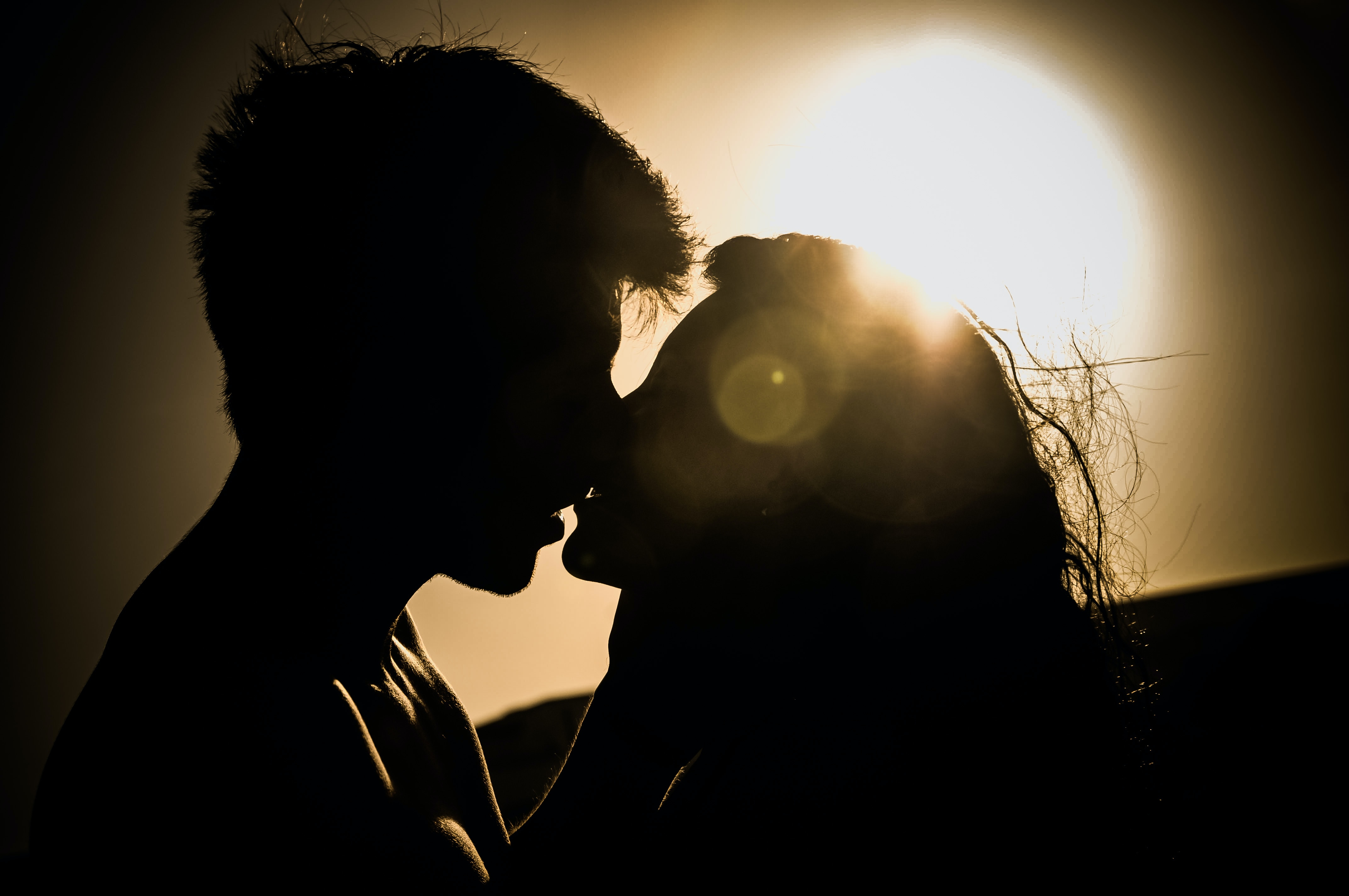 Eine Silhouette eines Paares, das sich vor der Sonne küsst.