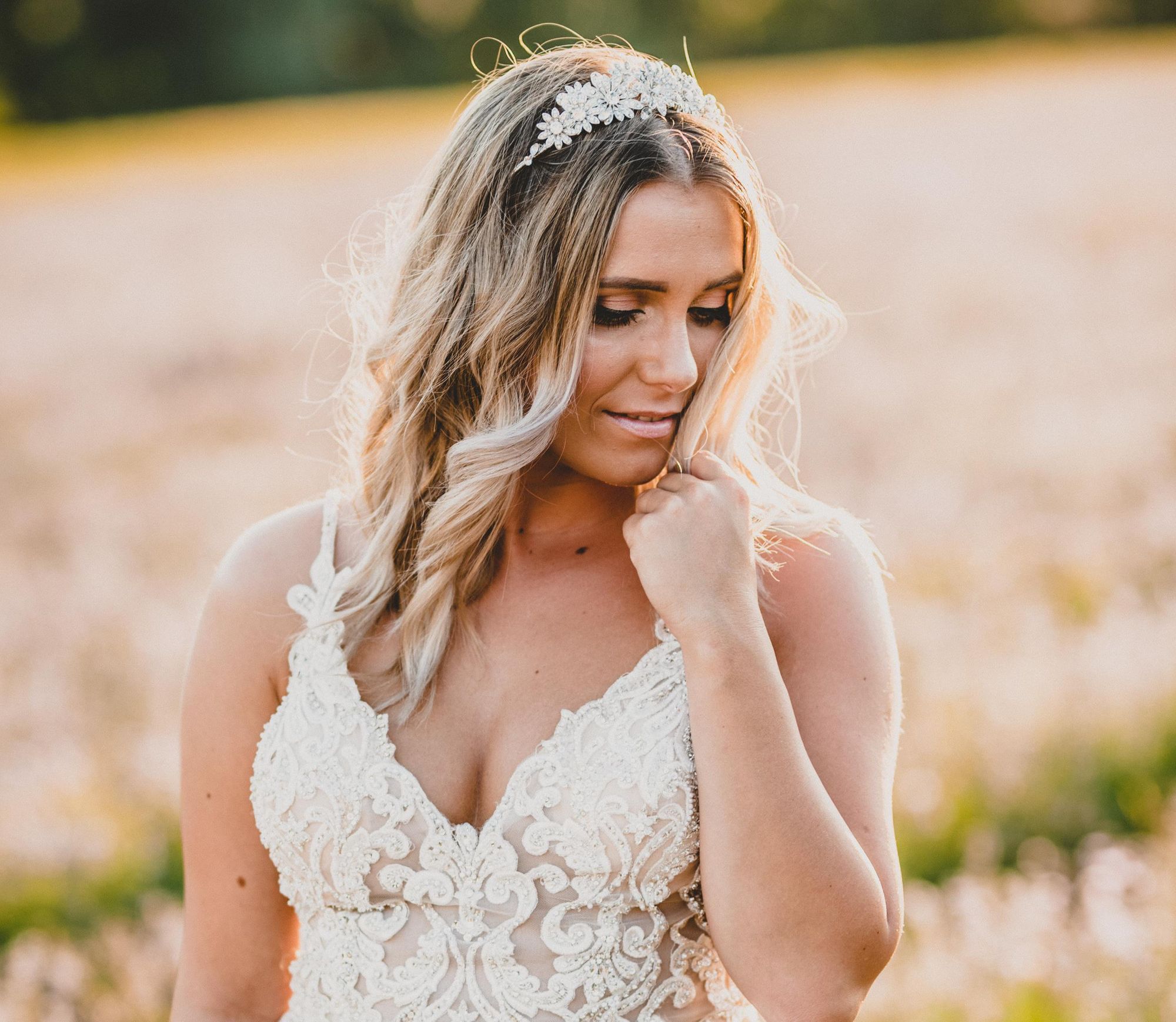 Eine Braut in einem Spitzenhochzeitskleid steht auf einem Feld.