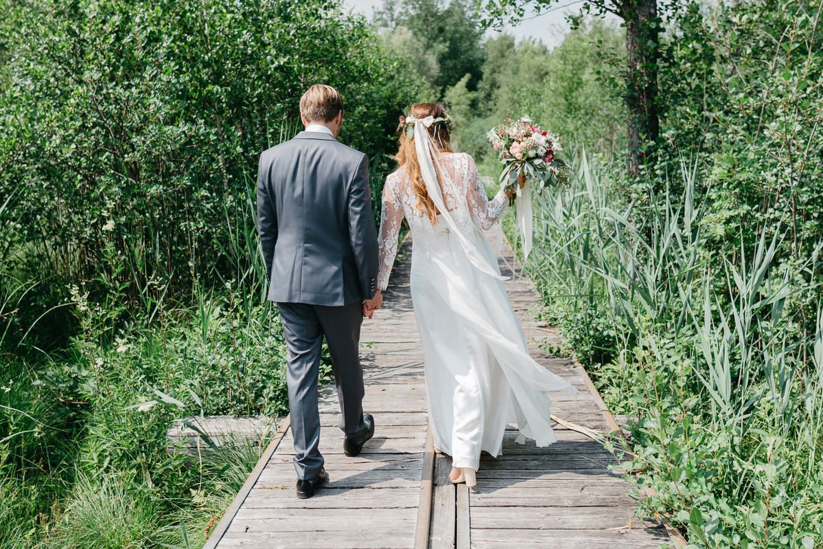 Eine Braut und ein Bräutigam gehen einen Holzsteg im Wald entlang.