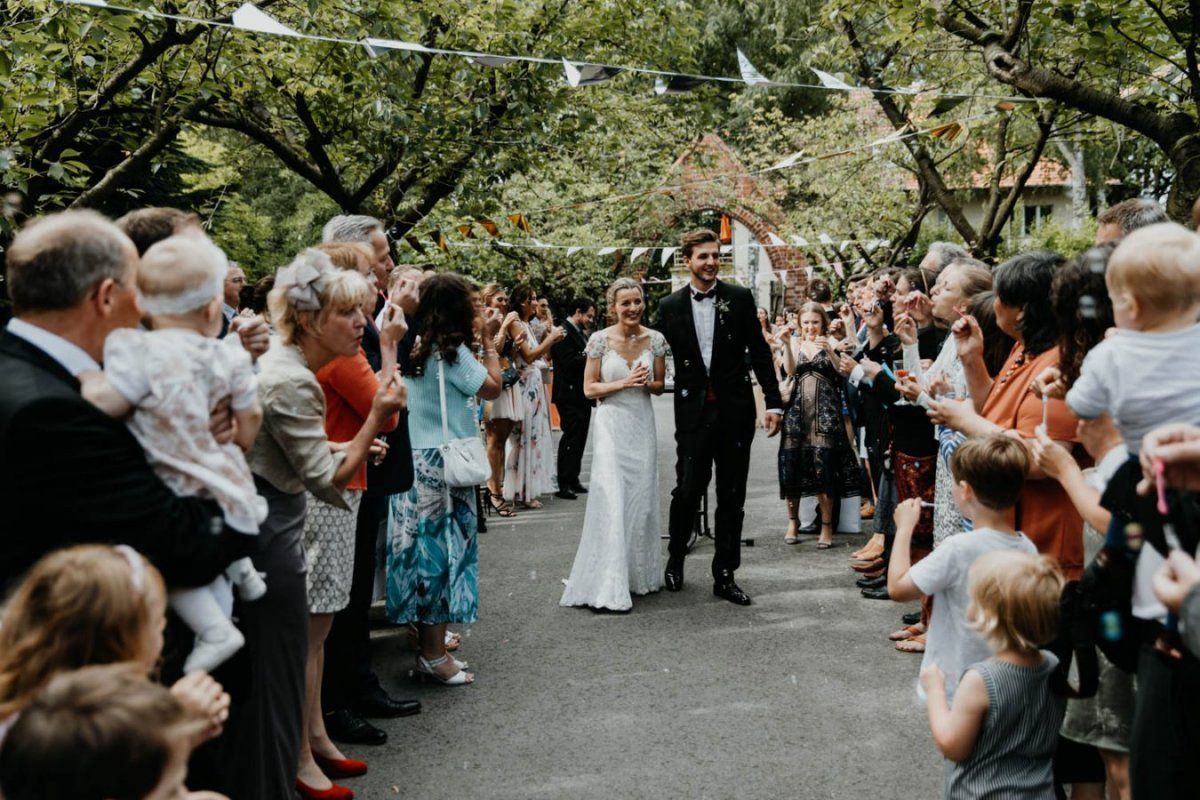 Ein Mann und eine Frau in einem Hochzeitskleid gehen mit einer Menschenmenge eine Straße entlang.