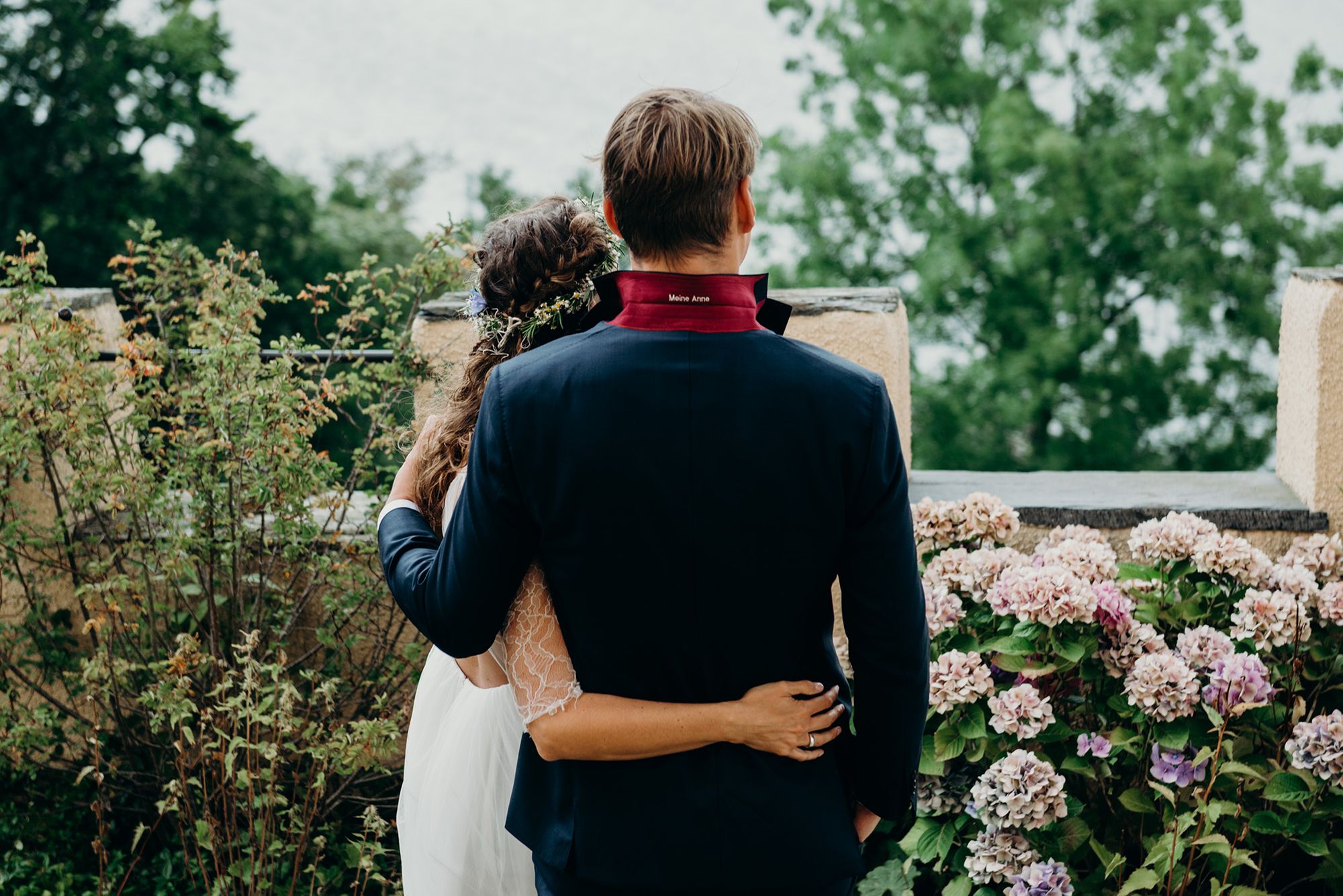 Eine Braut und ein Bräutigam stehen auf einem Balkon mit Blick auf einen See.