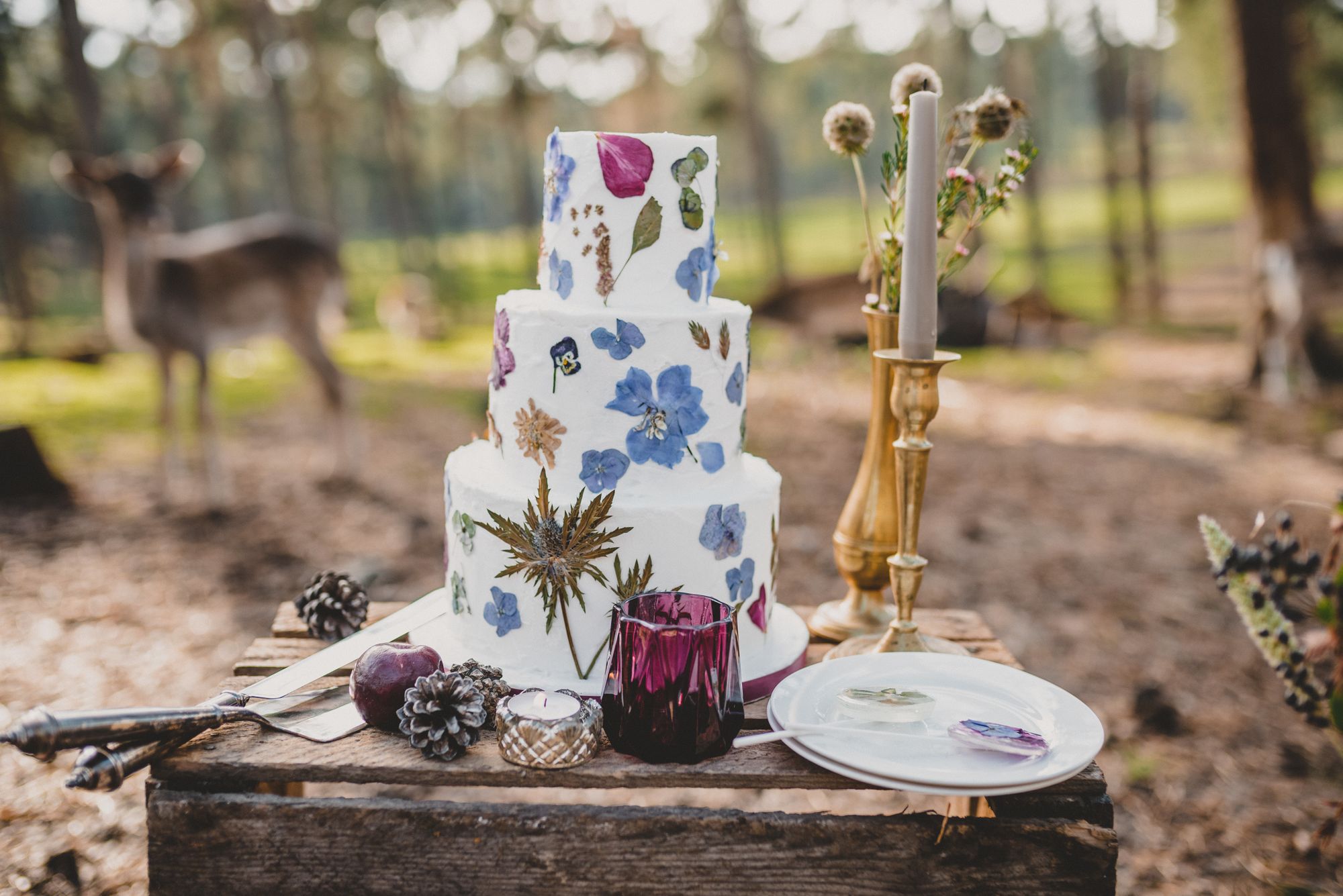 Eine Hochzeitstorte im Wald mit Hirschen und Blumen.