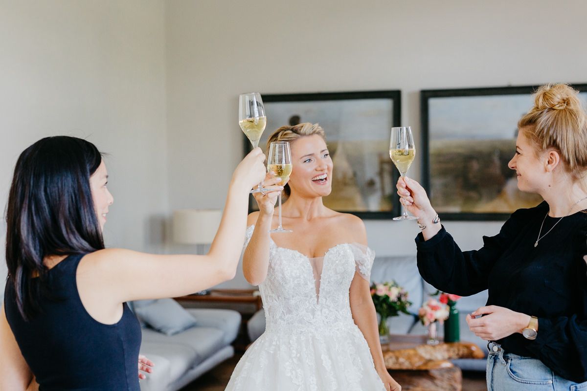 Eine Braut und ihre Brautjungfern stoßen im Wohnzimmer mit Champagner an.