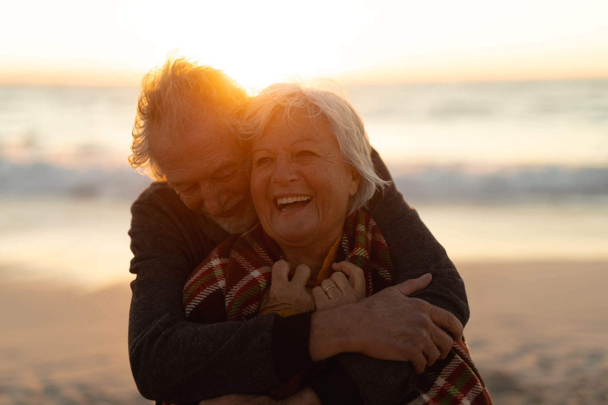 Ein älteres Paar umarmt sich bei Sonnenuntergang am Strand.