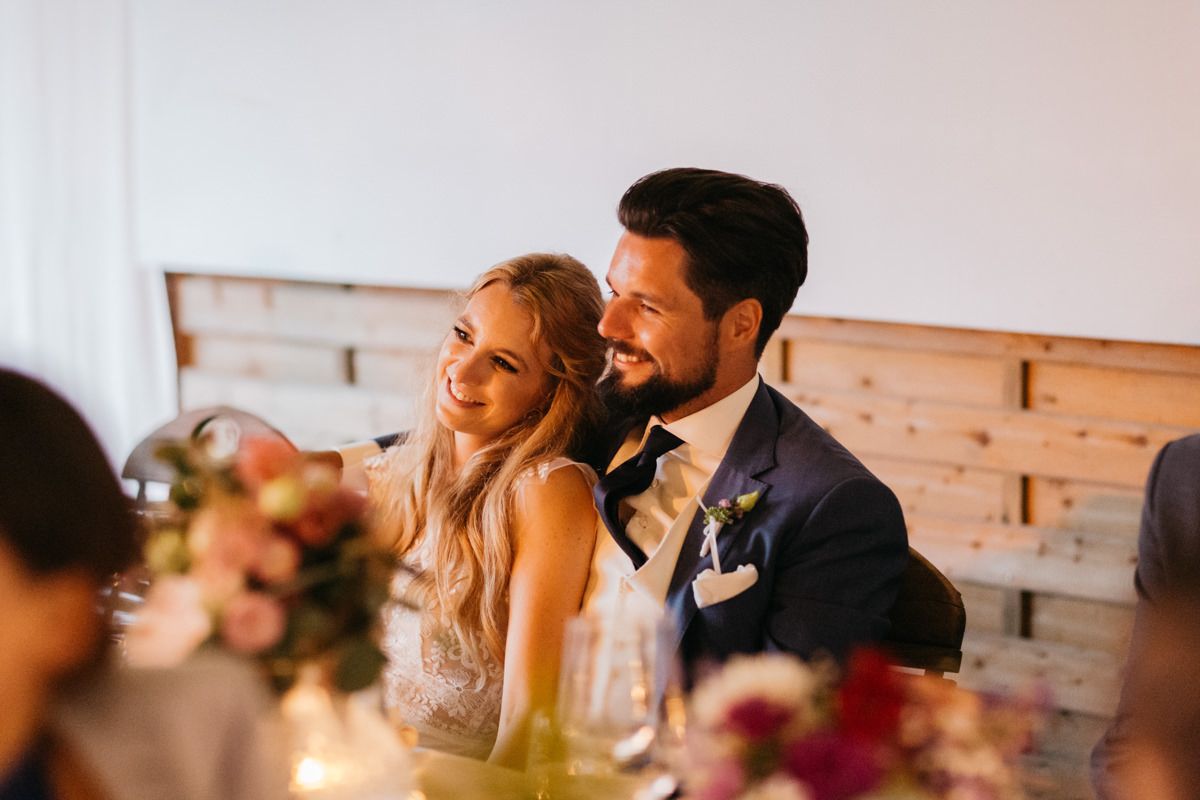Eine Braut und ein Bräutigam lächeln sich bei einer Hochzeitsfeier an.